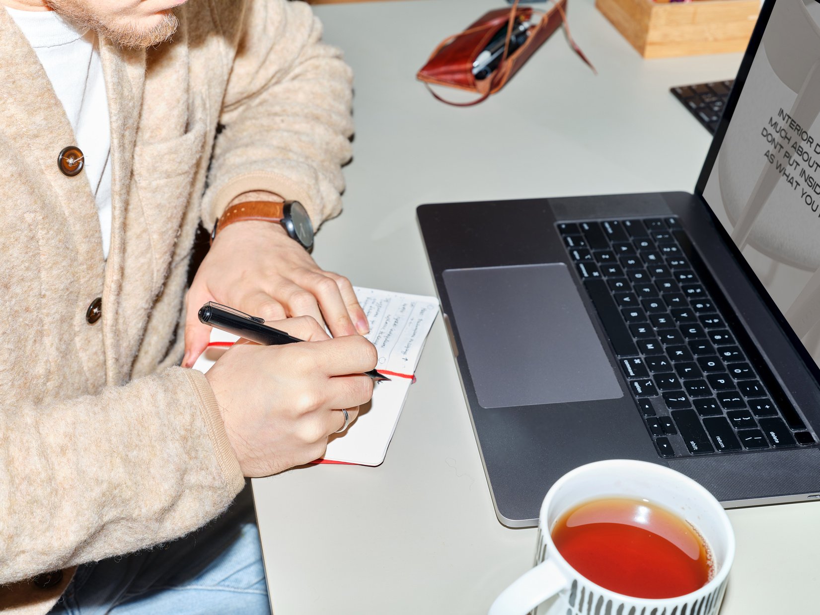 Graphic Designer Writing Notes While Working on a Laptop